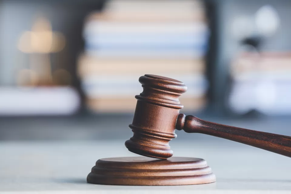A wooden gavel with gray background filled with a stack of books.
